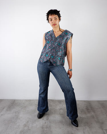 a woman is weariang a colorful vintage vest with geometric pattern in teal and pink by vinti vintage.