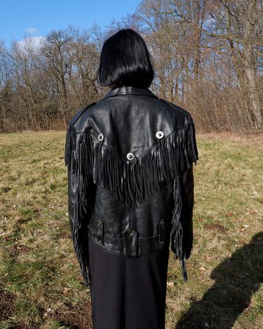 Add some wild vibes to your wardrobe with this vintage 80s 90s black fringe leather jacket. Complete with conchos and a belt, this jacket will be a statement piece for any outfit.