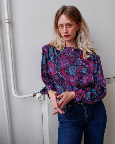 Lookin' for a way to make some '80s style magic? Slip on this vintage purple floral blouse with light shimmering accents and shoulder pads for a look that sparkles!