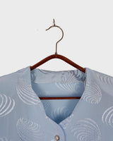 Introduce some sparkle to your style with this vintage 80s light blue blouse. The flattering fit, courtesy of the short sleeves and shoulder pads, meets a playful touch of shimmering pattern. Sparkle on!