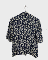 Get ready to channel some serious 90s romance with this vintage navy blue floral blouse with its light shimmering optic. Crafted from a luxurious silk mix blend, it features golden buttons and a unique collar for some extra flair. Romance never goes out of style!