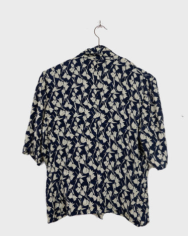Get ready to channel some serious 90s romance with this vintage navy blue floral blouse with its light shimmering optic. Crafted from a luxurious silk mix blend, it features golden buttons and a unique collar for some extra flair. Romance never goes out of style!