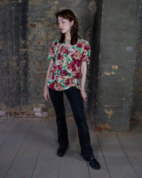 This vintage 1980s wrap blouse, crafted from luxurious pure silk, features a vibrant all-over rose print in rich red, pink, and green hues. The draped silhouette flows effortlessly, while a sculptural rose detail on the right side adds a bold, romantic twist. No tie needed – just slip it on and let the look speak for itself!
