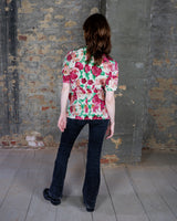 This vintage 1980s wrap blouse, crafted from luxurious pure silk, features a vibrant all-over rose print in rich red, pink, and green hues. The draped silhouette flows effortlessly, while a sculptural rose detail on the right side adds a bold, romantic twist. No tie needed – just slip it on and let the look speak for itself!