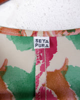 This vintage 1980s wrap blouse, crafted from luxurious pure silk, features a vibrant all-over rose print in rich red, pink, and green hues. The draped silhouette flows effortlessly, while a sculptural rose detail on the right side adds a bold, romantic twist. No tie needed – just slip it on and let the look speak for itself!