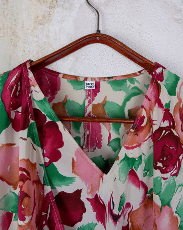 This vintage 1980s wrap blouse, crafted from luxurious pure silk, features a vibrant all-over rose print in rich red, pink, and green hues. The draped silhouette flows effortlessly, while a sculptural rose detail on the right side adds a bold, romantic twist. No tie needed – just slip it on and let the look speak for itself!