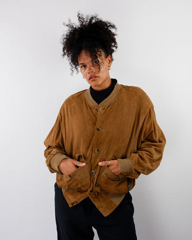 a woman is wearing a vintage 80s brown suede bomber jacket with light shoulder pads by vinti vintage