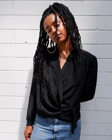 This classic vintage 90s black blouse has got you covered - literally! Wrap yourself up in this silky-smooth garment complete with shoulder pads and a fun floral pattern.