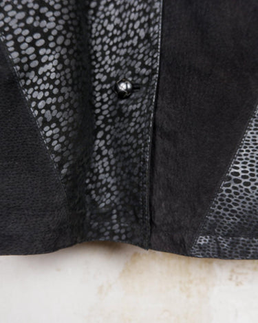 This vintage black leather coat blends matte suede leather with subtly glossy smooth leather panels in rich black tones. The unique patchwork design, featuring delicate dot-textured sections, adds depth, texture, and quiet individuality. With its sleek cut, button front, and spacious pockets, this timeless piece is full of character – perfect for those who appreciate quality and one-of-a-kind style.