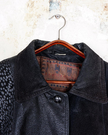 This vintage black leather coat blends matte suede leather with subtly glossy smooth leather panels in rich black tones. The unique patchwork design, featuring delicate dot-textured sections, adds depth, texture, and quiet individuality. With its sleek cut, button front, and spacious pockets, this timeless piece is full of character – perfect for those who appreciate quality and one-of-a-kind style.