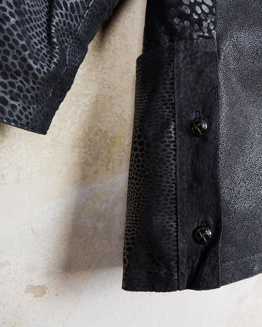 This vintage black leather coat blends matte suede leather with subtly glossy smooth leather panels in rich black tones. The unique patchwork design, featuring delicate dot-textured sections, adds depth, texture, and quiet individuality. With its sleek cut, button front, and spacious pockets, this timeless piece is full of character – perfect for those who appreciate quality and one-of-a-kind style.