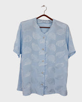 Introduce some sparkle to your style with this vintage 80s light blue blouse. The flattering fit, courtesy of the short sleeves and shoulder pads, meets a playful touch of shimmering pattern. Sparkle on!