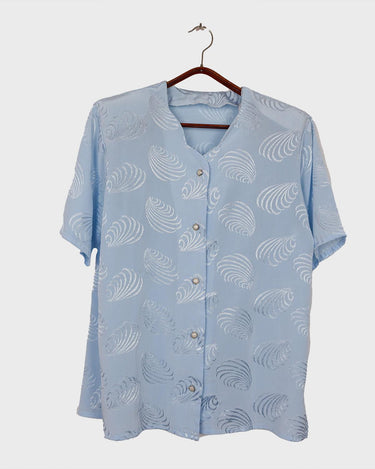 Introduce some sparkle to your style with this vintage 80s light blue blouse. The flattering fit, courtesy of the short sleeves and shoulder pads, meets a playful touch of shimmering pattern. Sparkle on!