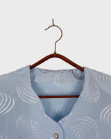 Introduce some sparkle to your style with this vintage 80s light blue blouse. The flattering fit, courtesy of the short sleeves and shoulder pads, meets a playful touch of shimmering pattern. Sparkle on!