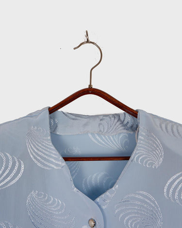Introduce some sparkle to your style with this vintage 80s light blue blouse. The flattering fit, courtesy of the short sleeves and shoulder pads, meets a playful touch of shimmering pattern. Sparkle on!