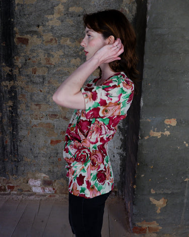 This vintage 1980s wrap blouse, crafted from luxurious pure silk, features a vibrant all-over rose print in rich red, pink, and green hues. The draped silhouette flows effortlessly, while a sculptural rose detail on the right side adds a bold, romantic twist. No tie needed – just slip it on and let the look speak for itself!
