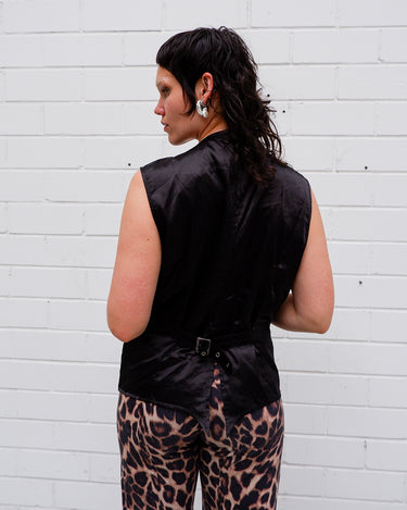 This Y2k black vest blends classic baroque style with a subtle gothic edge. The textured floral pattern and fleur-de-lis buttons give it a refined yet bold character. Cool, confident and a little unexpected – a standout piece without shouting.
