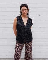 This Y2k black vest blends classic baroque style with a subtle gothic edge. The textured floral pattern and fleur-de-lis buttons give it a refined yet bold character. Cool, confident and a little unexpected – a standout piece without shouting.