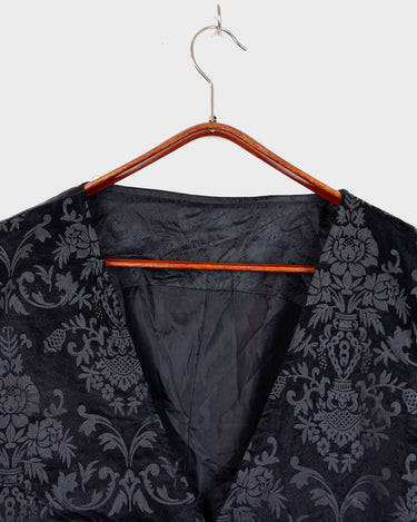 This Y2k black vest blends classic baroque style with a subtle gothic edge. The textured floral pattern and fleur-de-lis buttons give it a refined yet bold character. Cool, confident and a little unexpected – a standout piece without shouting.