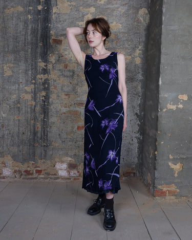 a woman is wearing a black maxi dress. This dress is hard to forget. Black meets bold violet florals in a print that feels dreamy, romantic, and just a little bit fairy. The silhouette flows with effortless ease. 90s elegance at its best.