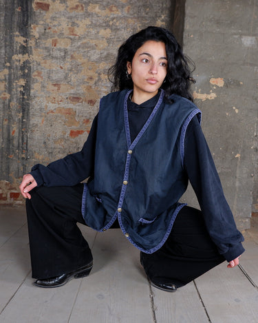 This elegant vintage vest from the 90s showcases a rich navy hue enhanced by subtly contrasting trim, creating a refined and timeless aesthetic. Likely crafted from cotton, it offers both durability and comfort while maintaining an effortlessly look.