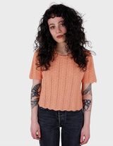 a woman with curly hair is wearing a salmon colored handmade shirt.