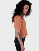 a woman with curly hair is wearing a salmon colored handmade shirt.