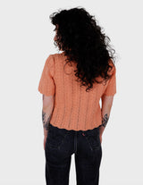 a woman with curly hair is wearing a salmon colored handmade shirt.