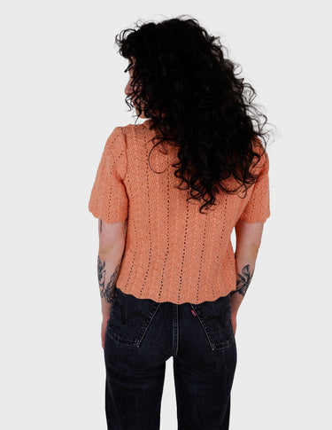 a woman with curly hair is wearing a salmon colored handmade shirt.