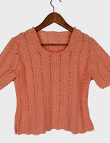 a woman with curly hair is wearing a salmon colored handmade shirt.