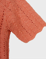 a woman with curly hair is wearing a salmon colored handmade shirt.