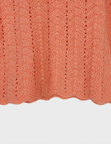 a woman with curly hair is wearing a salmon colored handmade shirt.