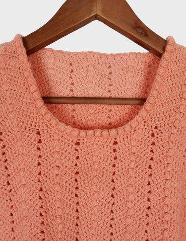 a woman with curly hair is wearing a salmon colored handmade shirt.