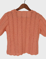 a woman with curly hair is wearing a salmon colored handmade shirt.