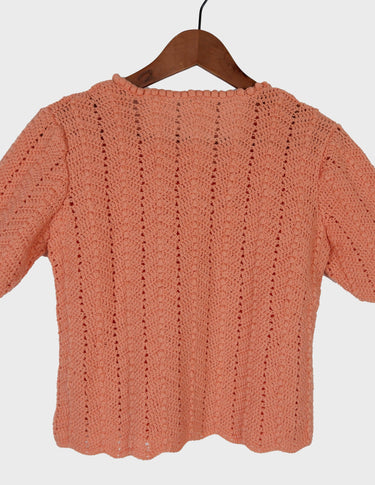 a woman with curly hair is wearing a salmon colored handmade shirt.